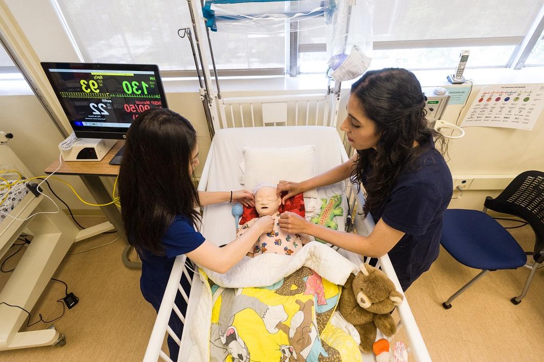 两个穿着手术服的护生在婴儿床里的娃娃上练习技能.